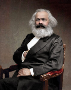 Karl Marx sitting in a chair, hand in suit, posing for a portrait circa 1875.